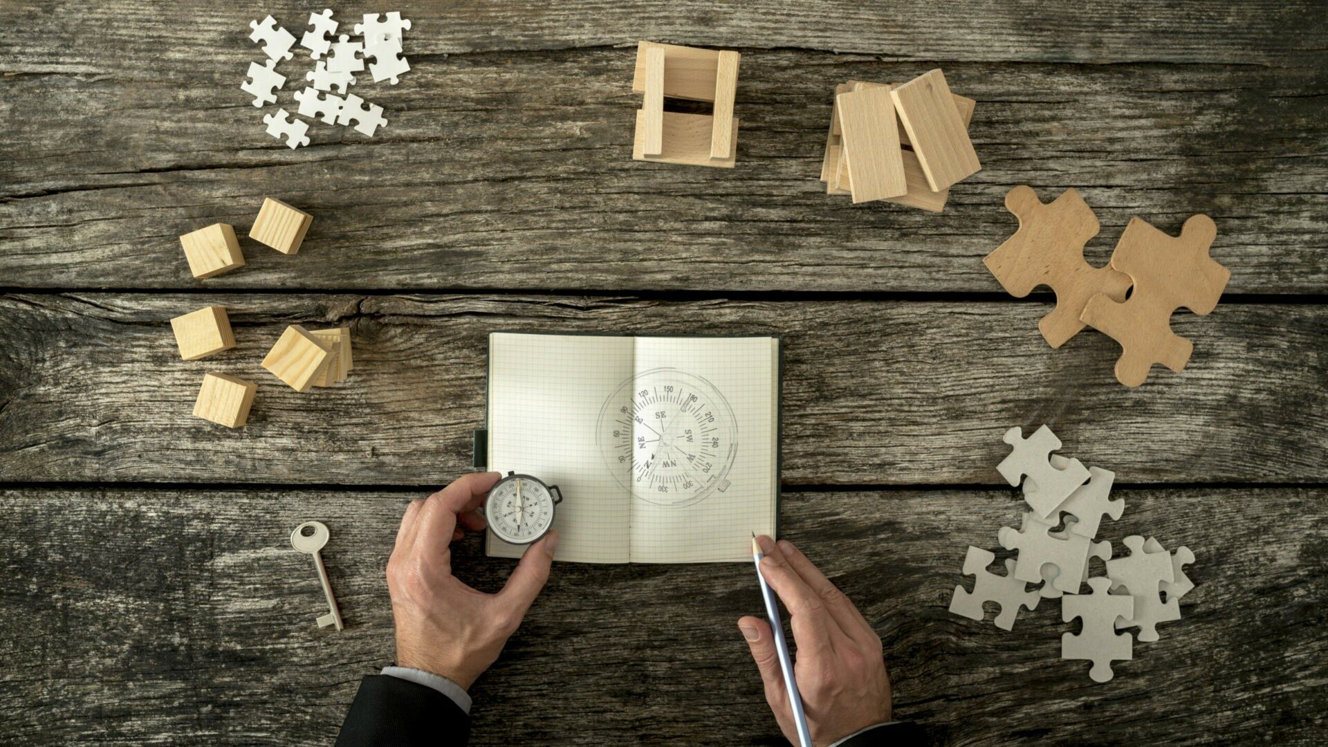 Businessman making plan and business strategy decisions as he sk Sicht von oben auf ein Notizblock, in das ein Kompass gezeichnet ist. Ein Mann hält einen Kompass daneben. Puzzleteil sind rundherum angeordnet.