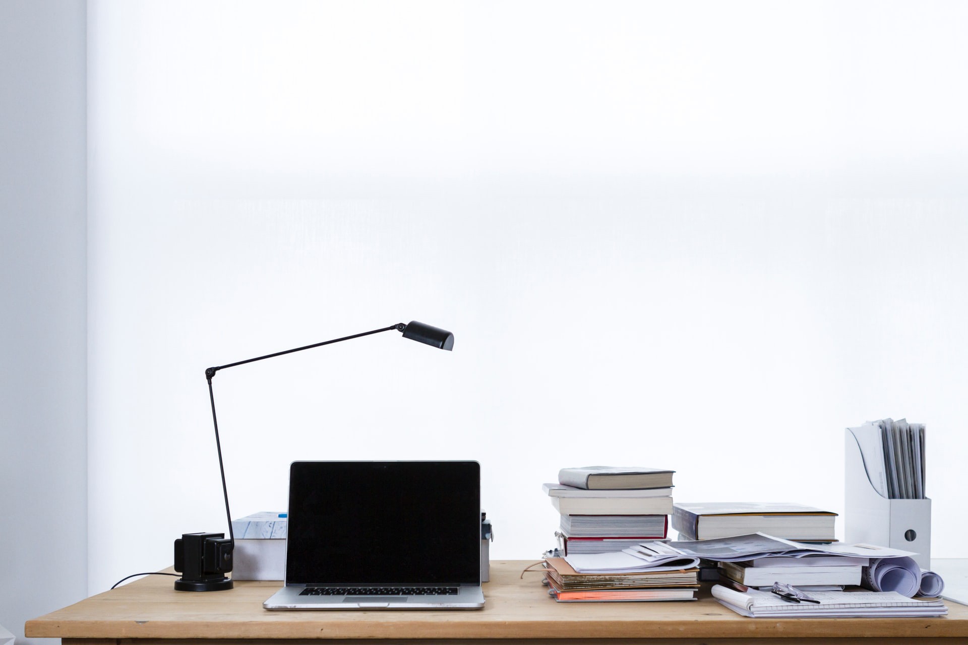 Recherche Foto eines Schreibtischs, auf dem ein Laptop sowie Bücher, Dokumente und Ordner liegen.